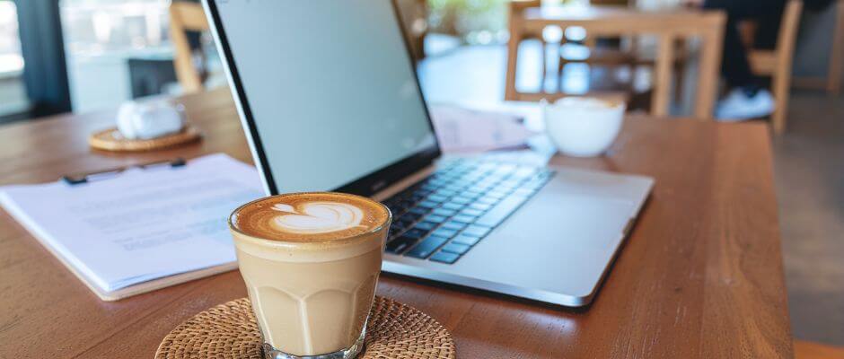 notebook sobre a mesa, com uma xicara de capucino ao lado